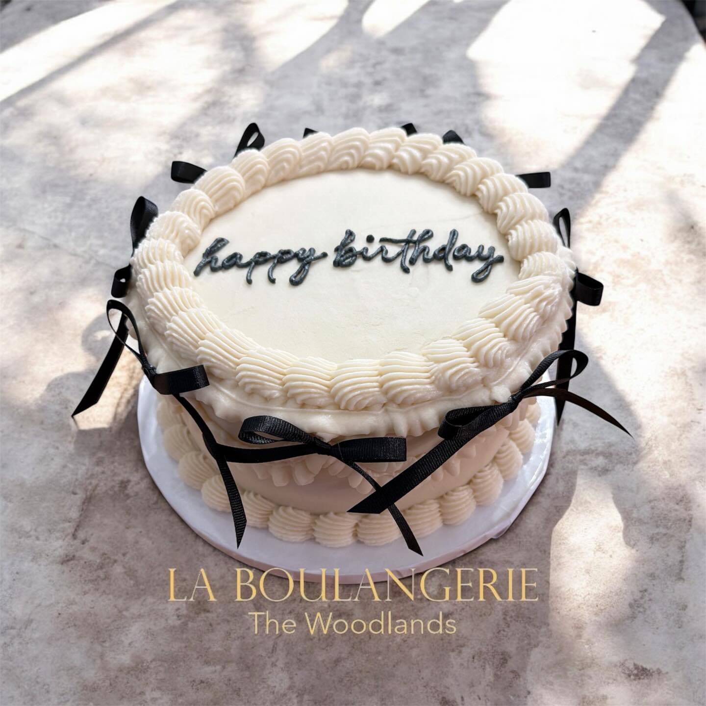 Elegant white birthday cake with piped buttercream and black ribbon bows