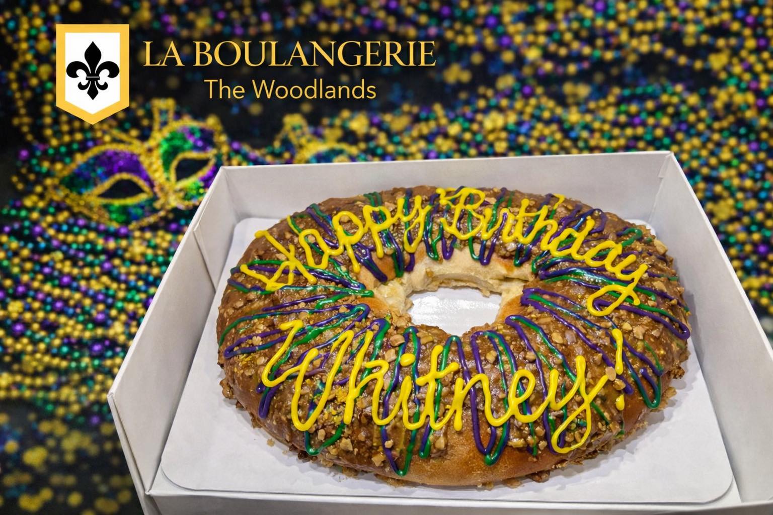 A Mardi Gras king cake with Happy Birthday written in icing, with purple, green, and gold decorations